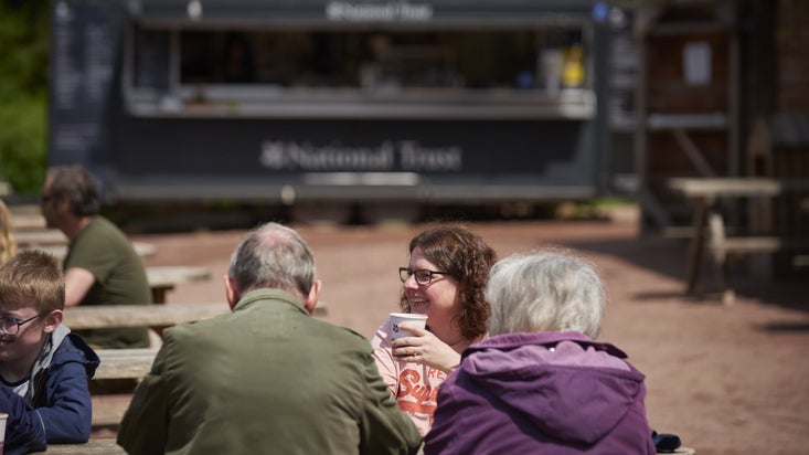 A family group sits at a picnic table outside a National Trust Cafe